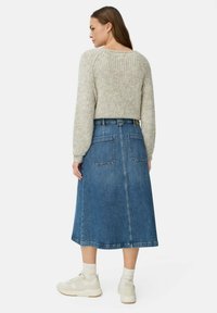 Pull en laine gris clair à cropped avec un tissu texturé, associé à une jupe en denim bleue de mi-longueur avec deux poches arrière et une silhouette droite.