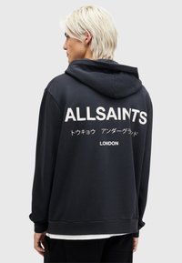 Felpa con cappuccio nera con il testo bianco "ALLSAINTS" e "LONDON" sulla schiena. Presenta una vestibilità rilassata e un tessuto morbido e testurizzato.