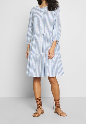 Vestito leggero a righe blu e bianche con maniche a tre quarti, chiusura frontale con bottoni, gonna a balze e vestibilità comoda. Abbinato a sandali marroni con cinturini.