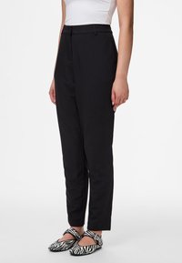 Calças pretas ajustadas com uma cintura alta e pernas afuniladas. Tecido suave com bolsos laterais, combinadas com sapatos rasos com padrão de zebra.