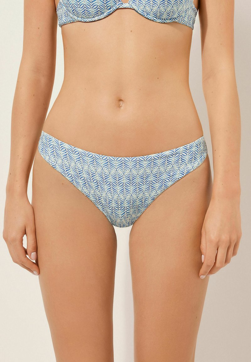 Bikini-topp i blå och krämfärgad bladmönster, gjord av mjukt tyg. Låg midja med en slät midjeband och minimal täckning.