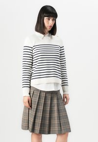 Gestreifter Pullover mit weißem Grund und marineblauen Streifen, kombiniert mit einem plissierten Karo-Rock in Grau- und Rosatönen.