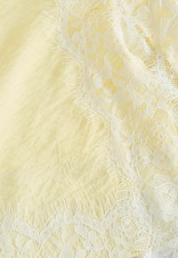 Tissu jaune avec une bordure décorative en dentelle florale blanche présentant des motifs complexes et des bords frangés.