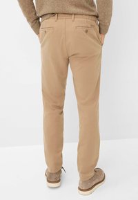 Beige katoenen broek met een rechte pasvorm, voorzien van achterzakken, subtiele stiksels, en gedragen met beige schoenen.