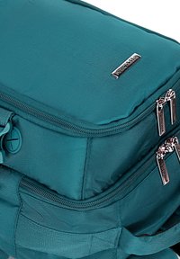 Turkusowy plecak z tkaniny z dwoma zamykanymi na zamek komorami, srebrnymi elementami metalowymi oraz fakturowanym materiałem. Posiada boczne i przednie kieszenie do przechowywania.