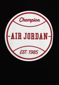Camiseta negra con un gran logo redondo blanco. Texto: "Champion", "AIR JORDAN" y "EST. 1985" en rojo. Diseño liso y audaz.