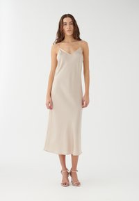 Robe nuisette en satin beige clair avec des fines bretelles ajustables et un décolleté en V, présentant un design fluide qui atteint le milieu du mollet.