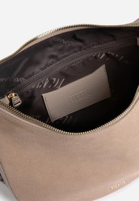 Interno di borsa in pelle color cuoio con una texture liscia, cerniera dorata e una piccola etichetta. Foderata con tessuto scuro con un marchio discreto.