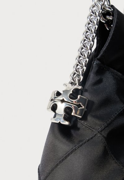 Ασημένιο φυλαχτό σε σχήμα σταυρού που κρέμεται από μια χοντρή ασημένια αλυσίδα προσαρτημένη σε μια μαύρη υφασμάτινη τσάντα.