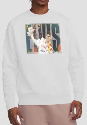 Man wearing white sweatshirt with an image of Elvis Presley waving and wearing a flower lei, with large "ELVIS" text overlay.