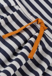 Streifenstoff in Marineblau und Weiß mit einer orangefarbenen Kordel, die am Bund zu einem Knoten gebunden ist.