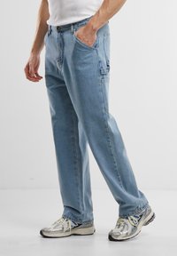 Lysblå denim jeans med en afslappet pasform, der har forlommer og subtile detaljer. Parret med sølvfarvede atletik sneakers.