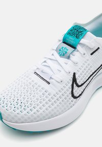 Nike tenisice za trčanje s bijelim mrežastim gornjim dijelom, tirkiznim naglascima, crnim šavovima i mekanim potplatom. Na jeziku se nalazi QR kod.