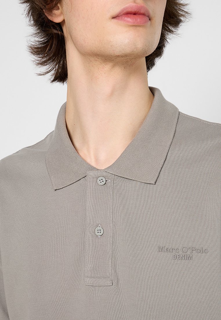 Helles grau Polo-Shirt aus strukturiertem Stoff, mit einem Drei-Knopf-Kragen und gesticktem "Marc O'Polo DENIM" Logo auf der Brust.