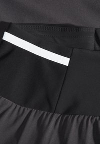 Gros plan sur un tissu noir avec un panneau en maille et un détail de bande blanche, montrant les coutures et une texture froncée.