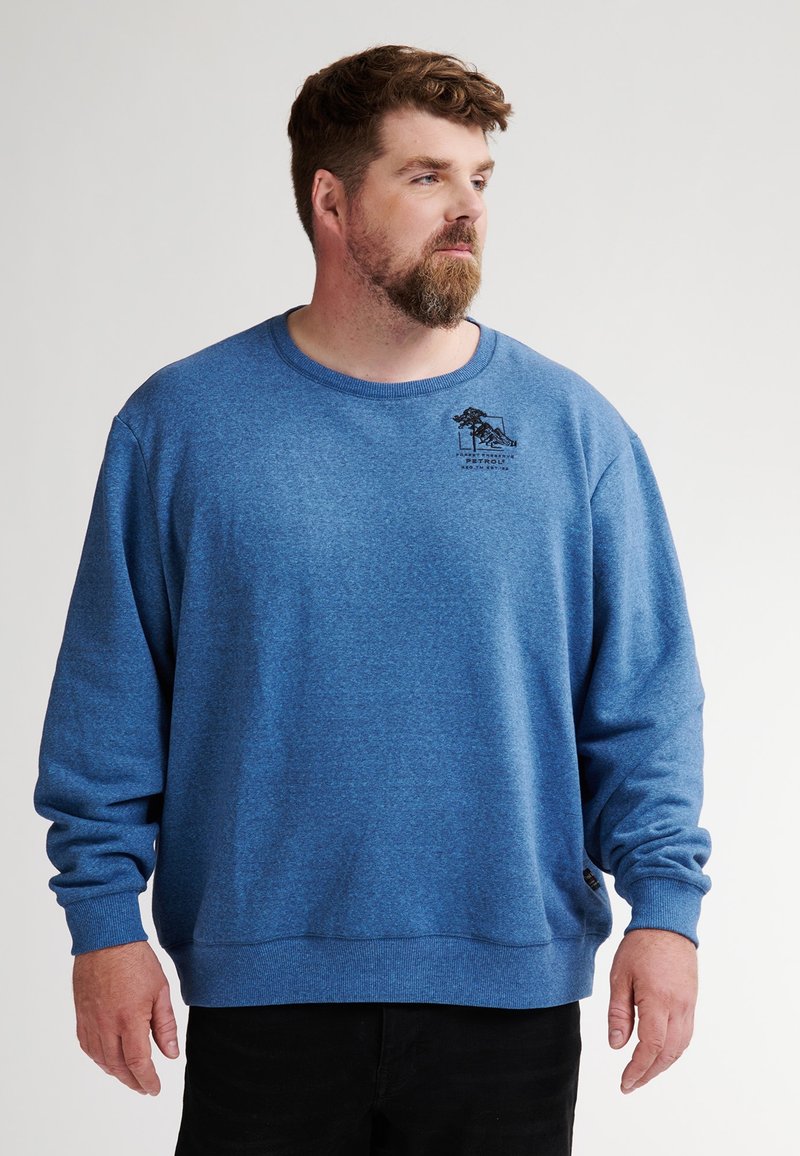 Sudadera de cuello redondo de forro polar azul con puños acanalados y un pequeño logo negro impreso en el pecho. Textura suave.