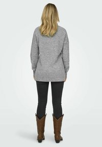 Suéter gris de corte holgado, con un dobladillo acanalado y mangas anchas, combinado con jeans oscuros y botas de vaquero marrones, visto desde la parte de atrás.