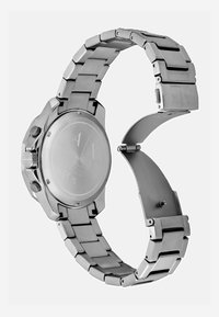 Hõbedane roostevabast terasest kell võrkbändiga. Omab ümmargust korpust, silmapaistvat kroonit ja tagaküljel graveeritud brändi logo.