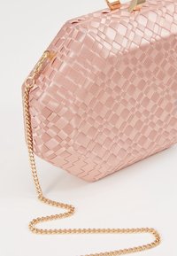 Pochette en satin rose avec fermoir doré et chaîne dorée attachée, posée sur une surface blanche.