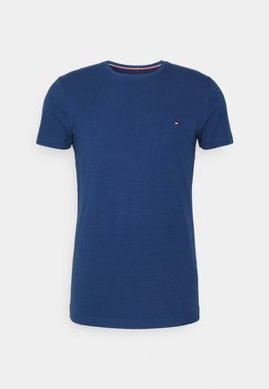 T-shirt uni bleu foncé à manches courtes et col rond avec un petit logo rectangulaire rouge, blanc et bleu sur la poitrine gauche.