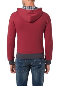 Felpa rossa con cappuccio e design cropped, polsini grigi e un rivestimento a quadri visibile nel cappuccio, abbinata a jeans blu.