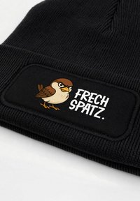 Black knitted beanie featuring a patch with a cartoon bird and the text "FRECH SPATZ." The material is ribbed, adding texture.