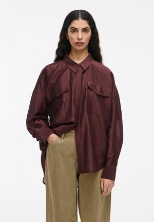 Bordeaux knopshirt met twee borstzakken, lose fit en lange mouwen. Glad oppervlak met een subtiele glans. Combinatie met beige broek.