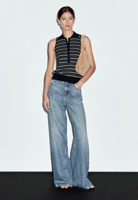 Ärmlös randig top i svart och vitt, parat med vida ljusblå jeans. Outfitten kompletteras med en tan axelväska.