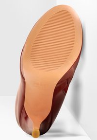 Semelle de chaussure rouge avec une finition lisse et brillante et une surface de préhension texturée de couleur beige clair. Présente une forme arrondie et un talon léger.