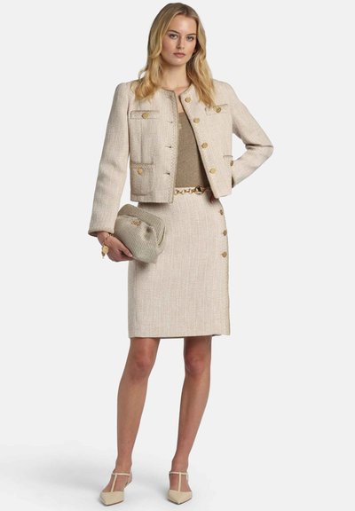 Beige tweed suit featuring a cropped jacket with gold buttons, paired with a pencil skirt and a matching clutch. Smooth texture and tailored fit.