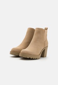 Beige Wildleder-Ankelboots mit Blockabsatz, elastischen Seitenpaneelen und einer robusten Sohle. Das Design zeichnet sich durch eine klare Silhouette und minimalistische Akzente aus.