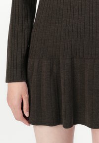 Abito lavorato a maglia marrone scuro con texture a coste, maniche lunghe e orlo svasato. Il tessuto è morbido e leggermente elasticizzato.