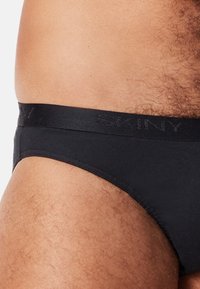 Zwarte katoenenslip met een zachte tailleband, met de merknaam "SKINY" in het midden geperst. Close-up van de materiaalt tekstuur en pasvorm.