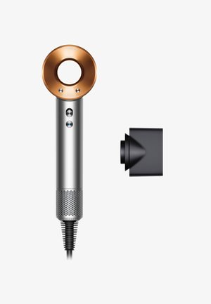 Sèche-cheveux avec un corps argenté, un inlet circulaire en cuivre, des boutons bleu et rouge, et un embout noir. Poignée texturée et cordon flexible.