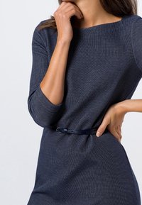 Tmavě modré úzké šaty se třičtvrtečními rukávy, texturovanou tkaninou a kontrastním úzkým páskem, který zvýrazňuje pás.