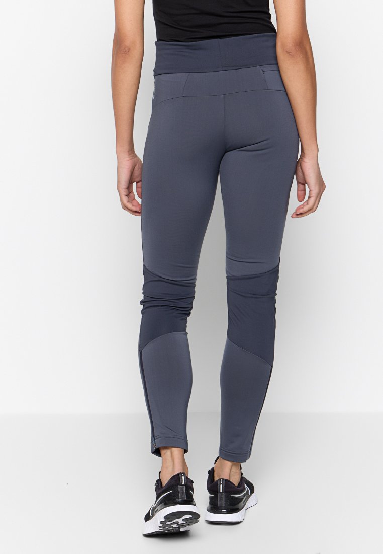 Graue Sportleggings mit hohem Bund, glatter Textur, eng anliegendem Design und Reißverschlüssen an den Knöcheln, kombiniert mit schwarzen Sportschuhen.