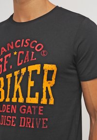 Camiseta de algodón negra con texto gráfico audaz y desgastado en rojo y amarillo: "San Francisco," "Biker," y "Golden Gate Paradise Drive."