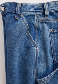 Blauwe spijkerbroek van denim met een vervaagde textuur, voorzien van een ritssluiting en zilverkleurige accenten, waaronder stervormige klinknagels en een ontwerp met vijf zakken.