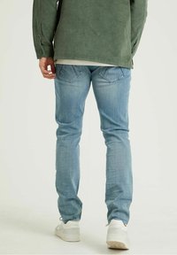 Vaaleansinisen farkkushortsien kapea istuvuus, hienovarainen haalistuma ja takataskut. Yhdistetty vihreään samettipaitaan, joka on jätetty paidan helma ulkopuolelle.