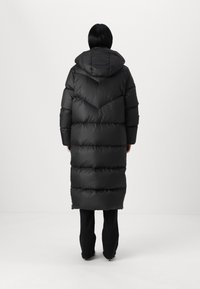 Long black puffer coat with a hood, featuring a chevron stitching pattern and horizontal sections. The fabric appears smooth and puffy.
