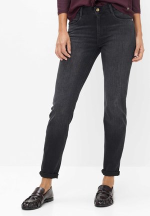 Person iført mørkegrå slim-fit jeans med opkaldte manchetter, mørkebrune læder loafers og en vinrød bluse med lange ærmer.
