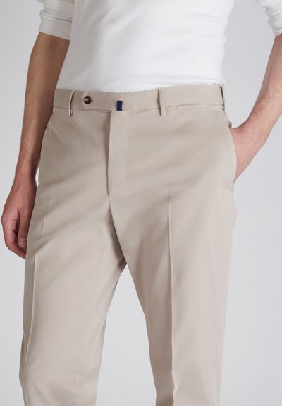 Pantaloni beige realizzati in un morbido tessuto misto cotone. Presentano una chiusura con bottone, tasche laterali e una vestibilità rilassata. Dettaglio di texture sottile.