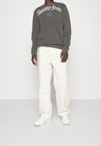 Šedá mikina s bílým logem "Tommy Jeans", doplněná krémovými kalhotami s širokými nohavicemi a bílými teniskami. Hladká textura látky.