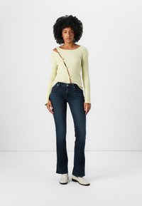 Ribbet lys grønn genser med én skulder design, side knapp detaljer; kombinert med mørkeblå utsvingte jeans og hvite ankelstøvler.