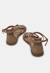 Béžové semišové sandály s páskem kolem kotníku, otevřenou špičkou a dekoračními stříbrnými akcenty. Plochá gumová podrážka se švy.