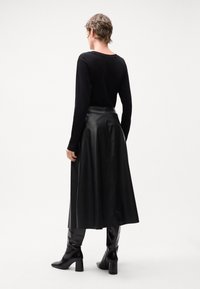 Sort langærmet top parret med en sort lænderedskørt, der har et flydende design og glat tekstur. Sorte knæhøje støvler fuldender outfittet.