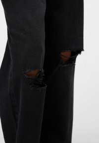 Zwarte denim jeans hebben een relaxte pasvorm met opvallende scheuren op de knieën, die rafelige randen en een oneffen textuur tonen.