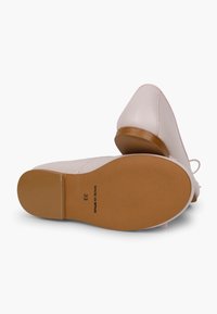 Chaussures en cuir rose clair avec un petit talon et une semelle en caoutchouc beige, présentant une texture lisse et des détails de couture minimaux. Fabriquées en Espagne.
