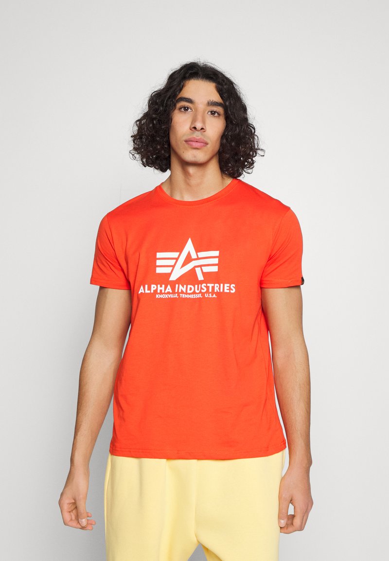 Rotes Baumwoll-T-Shirt mit einem auffälligen weißen "ALPHA INDUSTRIES"-Logo, rundem Halsausschnitt und kurzen Ärmeln. Glatte Textur mit lässigem Schnitt.