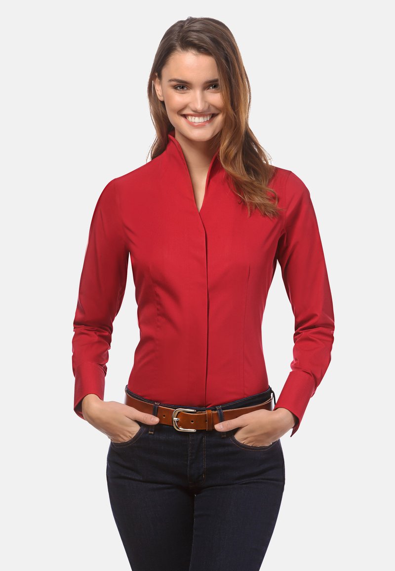 Chemise rouge à manches longues avec un col haut et des plis sur les côtés, faite d'un tissu lisse. Portez avec une ceinture marron sur un jean noir.